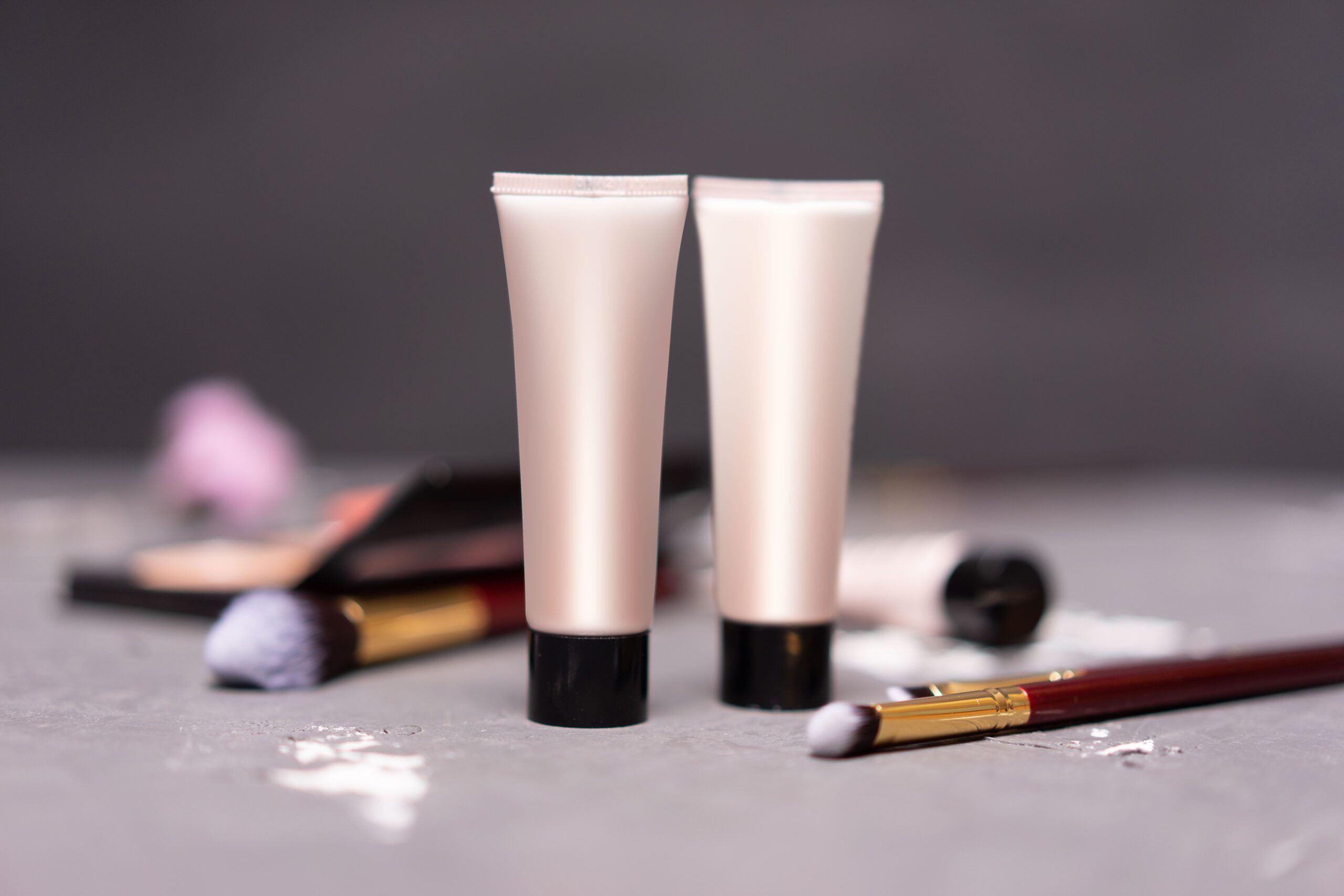 Close-up of skincare tubes with makeup brushes on a table, symbolizing beauty and self-care.